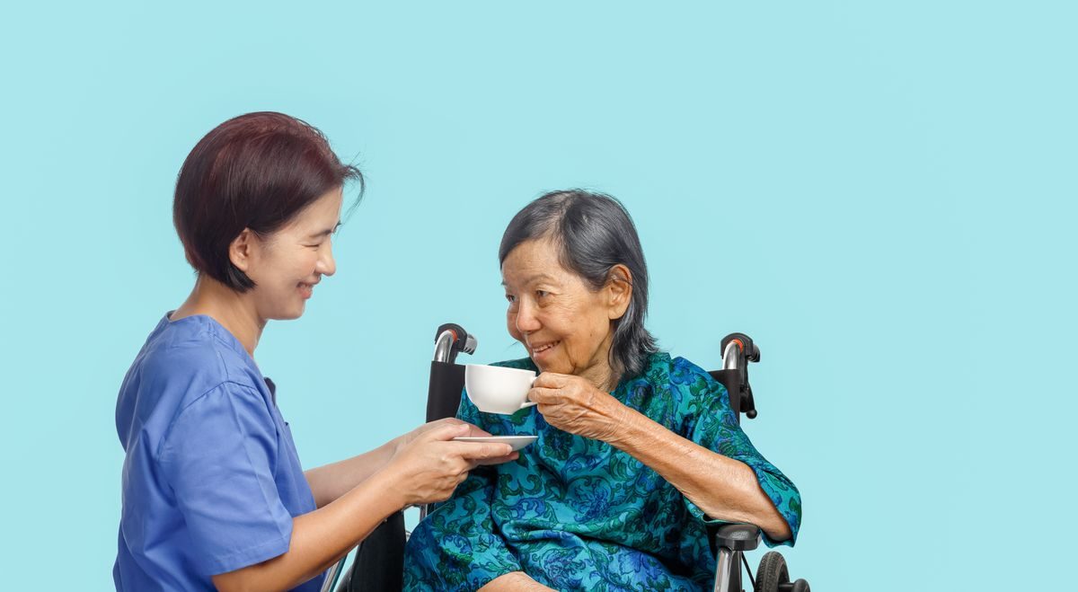 An older woman receiving a teacup from a caregiver